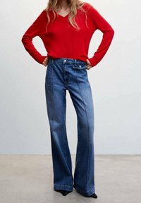 Rode v-hals trui gecombineerd met hoogzakelijke, wijde blauwe jeans met contrasterende stiksels en een gladde denimtextuur.