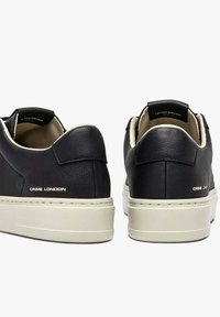 Sneakers nere in pelle con suole bianche, caratterizzate da una texture liscia, design minimalista e marchio sul tallone.