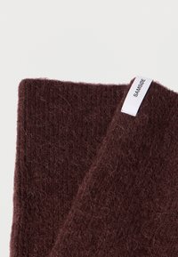 Viininpunainen villahuivi, jossa on teksturoitu, pörröinen pinta. Siinä on valkoinen bränditunniste, jossa lukee "SAMSØE." Suorakaiteen muotoinen, pehmeä ja lämmin.