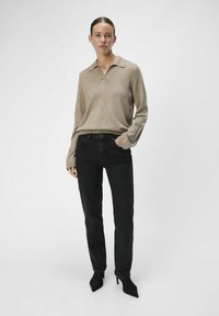 Top beige de manga larga con cuello, combinado con jeans negros de pierna recta y tacones negros puntiagudos. Diseño simple con un ajuste relajado.