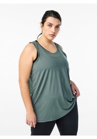 Tanktop in Dunkelgrün, aus glattem, leichtem Stoff. Mit rundem Ausschnitt und ärmellosem Design. Getragen mit schwarzen Sportleggings.