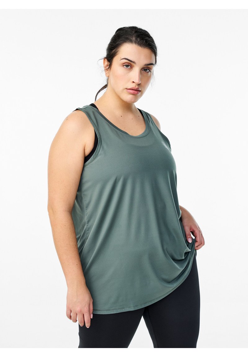 Tanktop in Dunkelgrün, aus glattem, leichtem Stoff. Mit rundem Ausschnitt und ärmellosem Design. Getragen mit schwarzen Sportleggings.