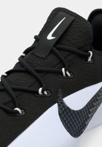 Μαύρο αθλητικό παπούτσι με υφασμάτινη επιφάνεια, λευκές δέστρες και μεγάλο μαύρο λογότυπο Nike. Διαθέτει λείο λευκό ενδιάμεσο σόλα και επενδυμένο κολάρο.