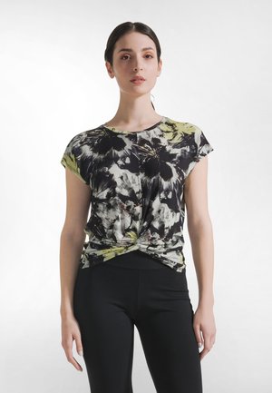 Floral-patterned short-sleeve top in black, green, and white, featuring a knotted front design. Paired with black leggings.