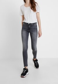 Jeans ajustados grises combinados con una camiseta de manga corta blanca. El calzado son zapatillas negras con detalles en blanco y rojo. Texturas de tela suaves visibles.