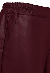 Bordeaux faux leren broek met een elastische tailleband en zichtbare zijzak met gedetailleerde stiksels.