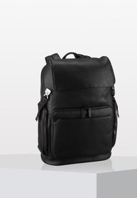 Zaino in pelle nera con texture liscia, scomparti con zip, spallacci regolabili e design minimalista. Presenta un dettaglio del logo sul davanti.