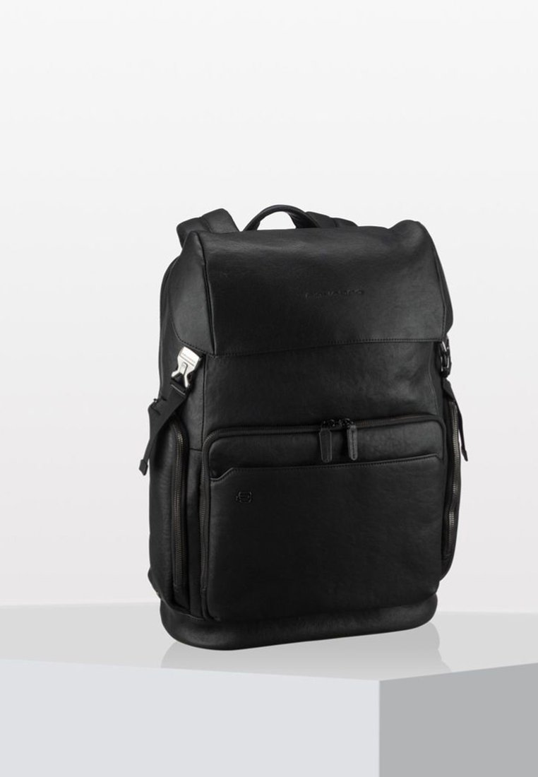 Zaino in pelle nera con texture liscia, scomparti con zip, spallacci regolabili e design minimalista. Presenta un dettaglio del logo sul davanti.