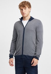 Sudadera con cremallera en azul marino y gris con un patrón de punto texturizado en diagonal. Presenta puños y cuello acanalados, y un diseño de corte regular.