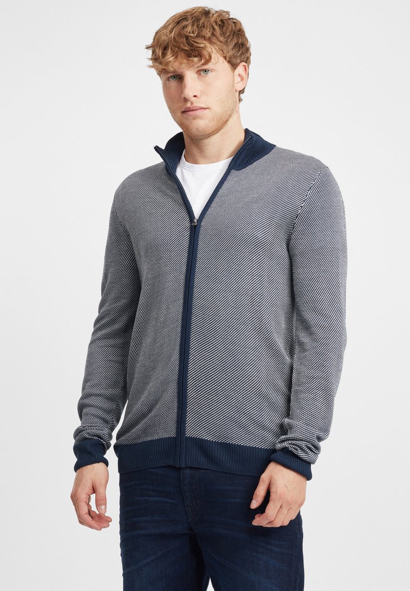 Sudadera con cremallera en azul marino y gris con un patrón de punto texturizado en diagonal. Presenta puños y cuello acanalados, y un diseño de corte regular.