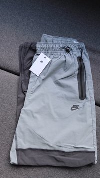 Lys grå og mørk grå Nike treningsshorts med elastisk midjebånd, sidelomme med glidelås og et merkevedheng. Glatt tekstur.
