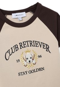 Camiseta de algodón de color crema y marrón con ribetes, con bordado del texto "CLUB RETRIEVER", un diseño de perro y detalles dorados. Presenta mangas raglán.