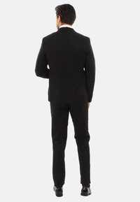 Completo formale nero con giacca su misura e pantaloni slim-fit, caratterizzato da una trama liscia e accenti coordinati, visto da dietro.