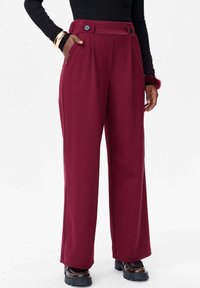 Wijdvallende bordeauxrode broek gemaakt van zachte stof, met twee voorkwamen, dubbele knoopsluiting en een hoge taille.