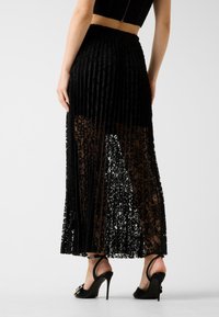 Gonna plissettata nera con sovrapposizione in pizzo, presenta sezioni trasparenti e una vita elasticizzata. Abbinata a sandali neri con tacco.