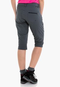 Pantalones cortos gris de longitud a la rodilla con una textura suave, que presentan un bolsillo con cremallera y puños enrollados. Combinados con zapatos de senderismo negros y calcetines grises.
