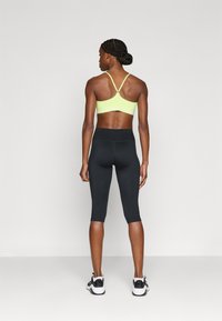 Κίτρινο αθλητικό μπράλετ με ρυθμιζόμενες τιράντες, συνδυασμένο με μαύρο κάπρι κολάν. Το σύνολο παρουσιάζει εφαρμοστή σχεδίαση και ομαλές υφές.