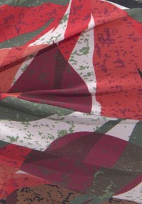 Keliamos spalvotos medžiagos, kurių geometrinis raštas apima raudonus, žalius ir baltus formas. Lygi tekstūra su lengvu blizgesiu.