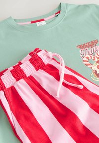 Mint green t-shirt with graphic print and short pink and red striped shorts with an elastic waistband and drawstring.