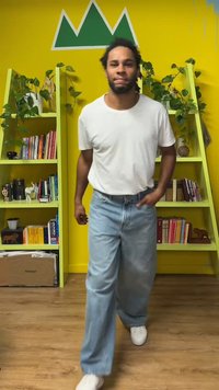 White t-shirt and light blue wide-leg jeans, walking on wooden floor, with bright yellow wall and green bookshelf in background.