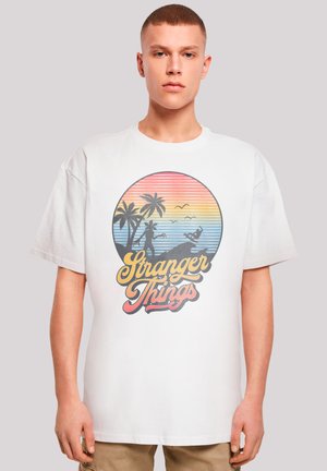 Weißes Baumwoll-T-Shirt mit einem bunten Grafikdesign eines Sonnenuntergangs über Palmen, mit "Stranger Things"-Text in Gelb und Pink.