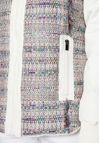 Chaqueta acolchada con tela de tweed multicolor que presenta un bolsillo con cremallera blanca. Superficie texturizada con hilos vibrantes en púrpura, verde y azul.