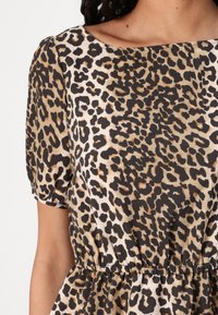 Blusa a maniche corte con stampa leopardata in beige e marrone, con scollatura rotonda e vita arricciata per una vestibilità comoda. Tessuto strutturato.
