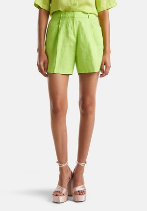 Shorts en lin vert citron avec des plis et une coupe ajustée, associés à des sandales compensées rose pâle avec un design à lanières.