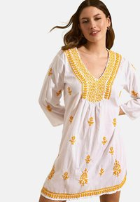 Robe blanche brodée avec des motifs floraux jaunes, décolleté en V et manches 3/4. Présente une broderie ornée le long de l'encolure et de l'ourlet.