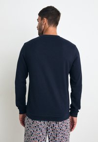 Marineblå sweatshirt med rund hals og lange ærmer, med en glat tekstur. Bæres med mønstrede pyjamasbukser.