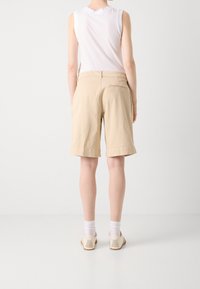 Shorts di cotone beige con una vestibilità rilassata, lunghezza al ginocchio, orlo risvoltato e una tasca posteriore. Indossati con una canotta bianca senza maniche e scarpe chiare.