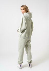 Felpa verde chiaro e pantaloni abbinati in tessuto morbido. La felpa presenta un cordino e grandi tasche; i pantaloni hanno una gamba affusolata e polsini elastici.