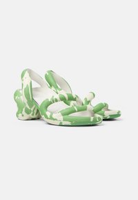 Green and white patterned slide sandals with a chunky heel and flexible material; features wavy straps and rounded toe design.