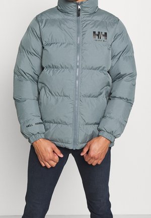 Polstret jakke i olivengrøn med høj krave, lynlås, elastiske ærmekanter og "Helly Hansen"-logo på brystet og ærmet.