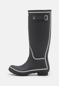 Hög svart gummiregnstövel med en slät yta, silverdetaljer och ett justerbart spänne. Har en räfflad sula för bra grepp.