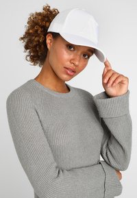 Cappellino da baseball bianco con logo "A" in rilievo, abbinato a un maglione grigio a maglia testurizzata con polsini a coste e scollo rotondo.
