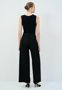 Zwarte mouwloze top gecombineerd met hoge taille, wijd broek en zwarte hoge hakken, gezien vanuit de achterkant. Eenvoudig ontwerp.