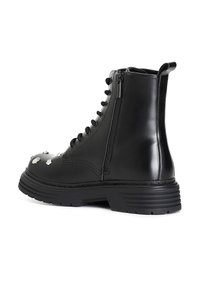 Botín negro de imitación cuero hasta el tobillo con suela gruesa, parte delantera con cordones, cremallera lateral y tachuelas metálicas decorativas en la zona del dedo del pie.