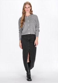 Cardigan gri tricotat cu textură în relief, având un guler rotund și nasturi în față, asortat cu o fustă lungă din denim negru, cu o deschidere frontală.