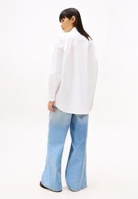Chemise blanche surdimensionnée à boutons, à manches longues, associée à un jean denim bleu clair à taille large, présentant une texture décolorée.