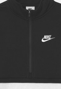 Černá mikina na zip z měkké látky. Má vysoký límec a bílé logo Nike na levé straně. Zapínání na přední zip.