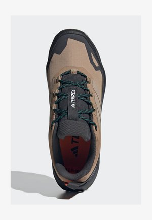 Terrex footwear in earthy brown with a textured fabric upper, black rubber sole, green laces, and a reinforced toe for durability.