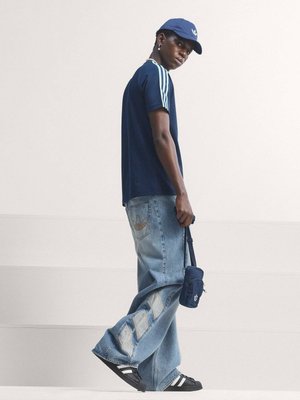 Young man in navy blue Adidas cap and shirt with light blue jeans, black Adidas sneakers, and holding a small navy blue bag.