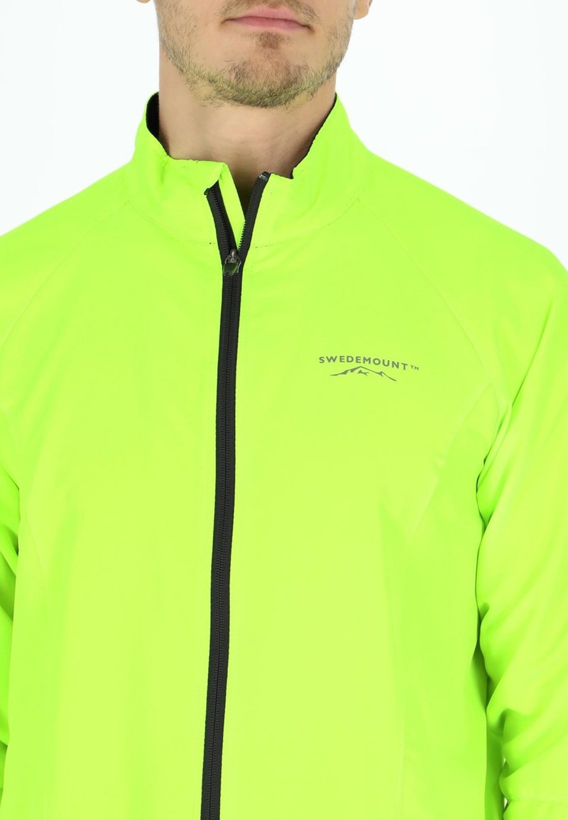 Fluorescerende grøn jakke, lavet af letvægtsmateriale. Har en høj krave, fuld lynlås og et subtilt logo på brystet.