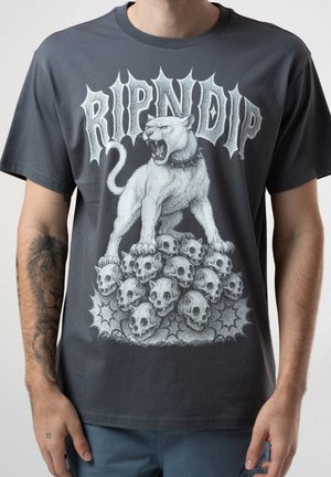 Rycząca biała pantera z kolczastą obrożą stojąca na stosie czaszek pod napisem "RIPNDIP" na ciemnoszarej koszulce.