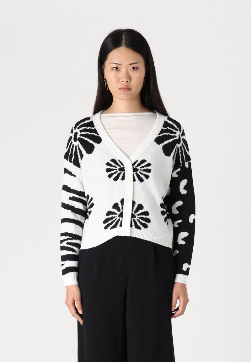 Cardigan tricoté noir et blanc avec des motifs floraux et abstraits, décolleté en V, fermeture à boutons et poignets côtelés. Design mi-court.