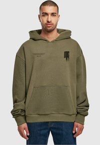 Olive green hoodie with spacious hood, front pocket, ribbed cuffs, and subtle black graphic details on the chest. Textured fabric.
