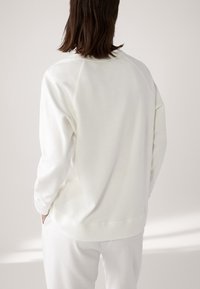 Witte sweatshirt met lange mouwen, voorzien van een ronde halslijn en raglanontwerp. Zachte textuur, ontspannen pasvorm en minimalistische stijl.