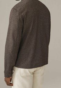 Bruin textuur shirt van geribbelde stof, met lange mouwen en een kraag. Gecombineerd met lichtgekleurde broek, wat een casual pasvorm toont.