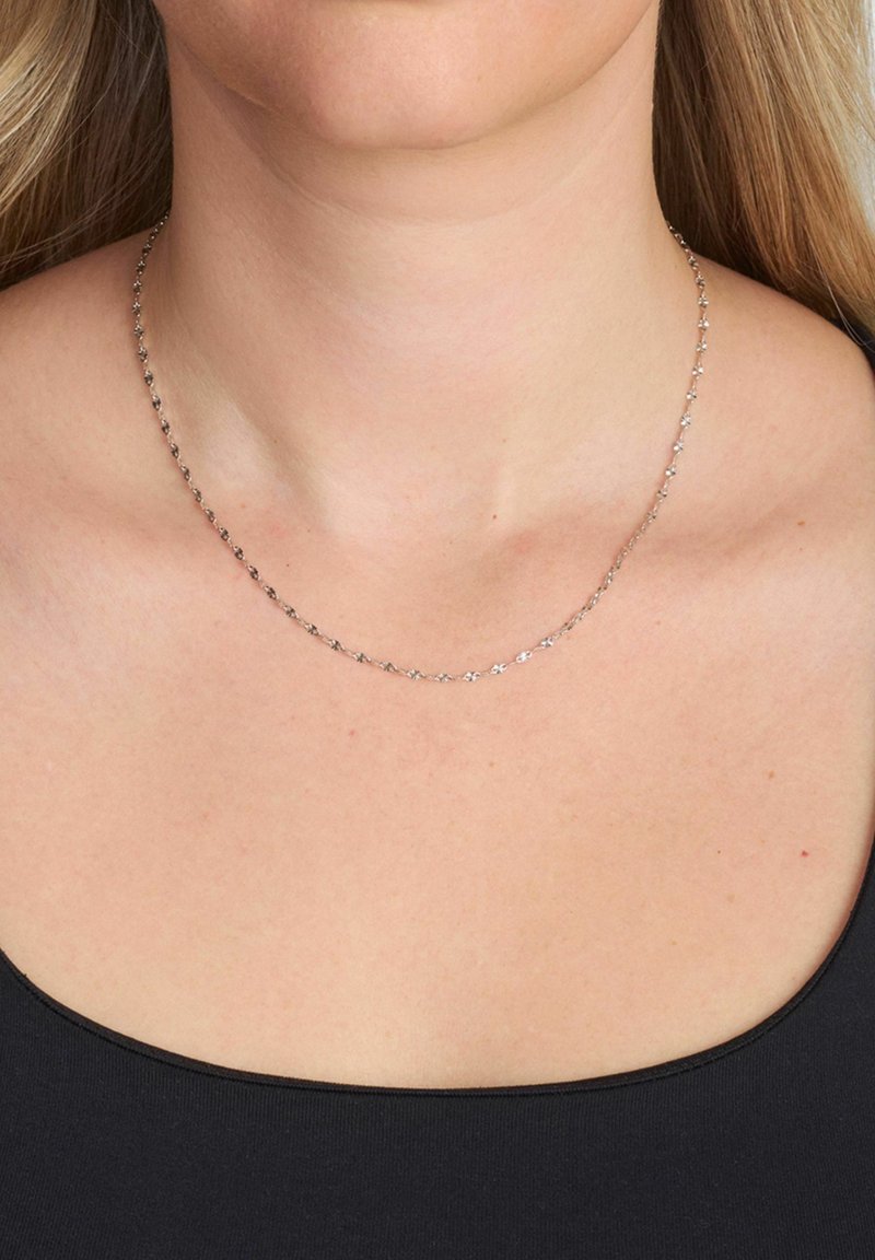Collier chaîne argent avec de petites attaches en forme de fleurs liées entre elles. Finition lisse et design délicat, porté au niveau de la clavicule.